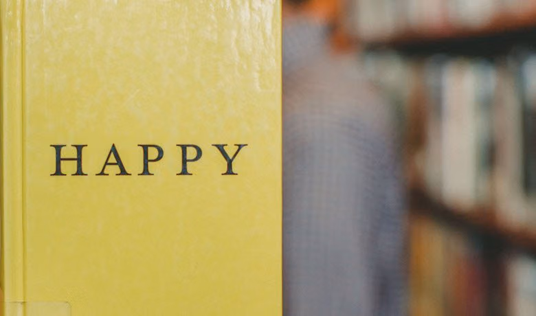 Yellow book with Happy printed on its cover in front of blurred library shelves