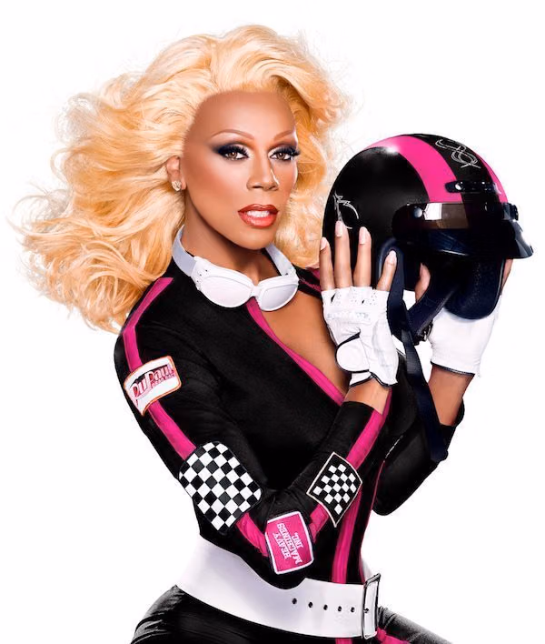 RuPaul in a black and pink racing suit holding a motorcycle helmet in a Drag Race promo