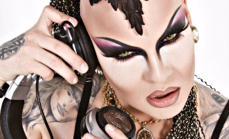 Nina Flowers in dramatic purple and black eye makeup, holding DJ headphones to her ear