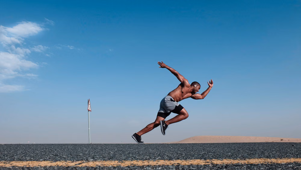 Shirtless man sprinting along a desert road under a clear blue sky
