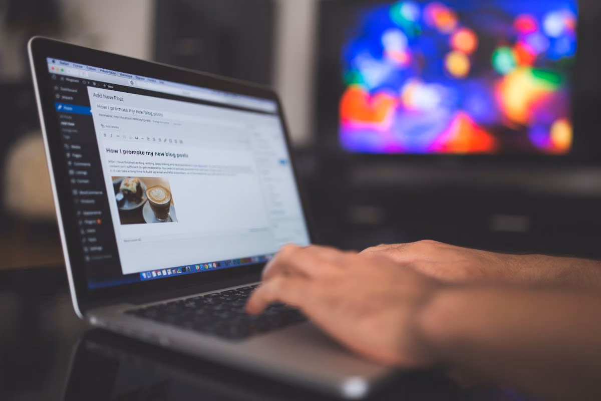 Hands typing on a laptop open to the WordPress Add New Post editor, with a draft blog post on screen