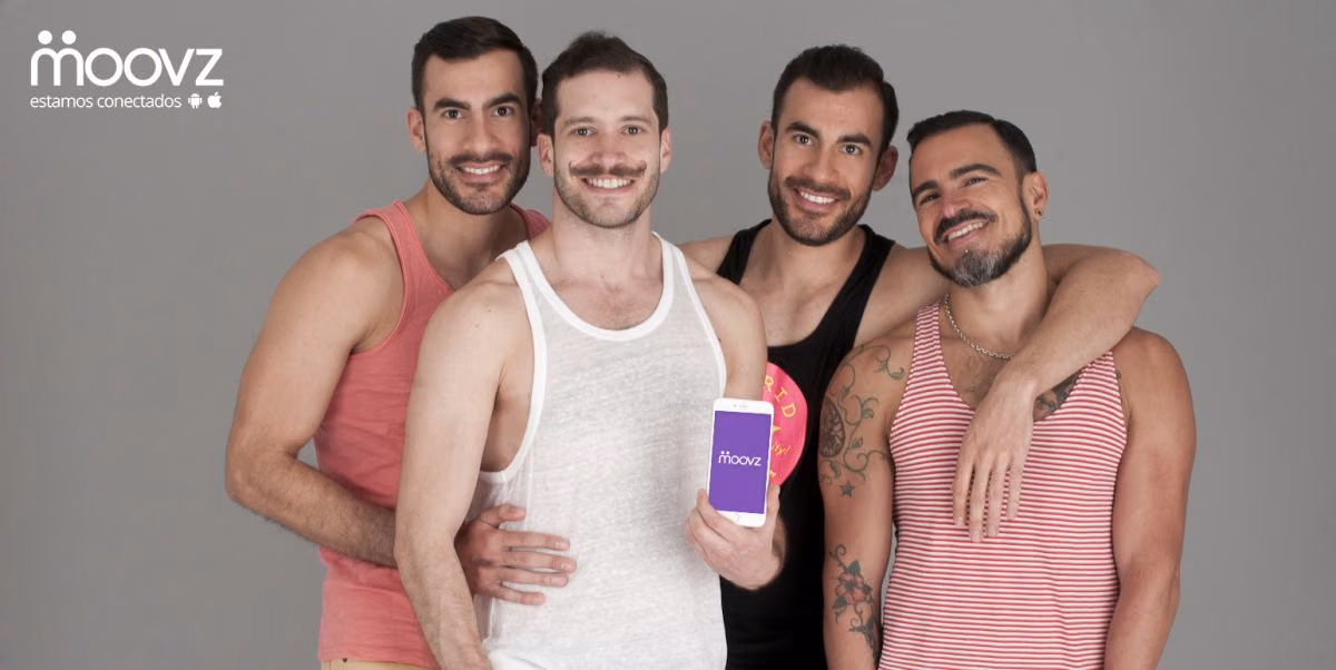 Four smiling men in tank tops, one holding a phone showing the Moovz LGBT social network app