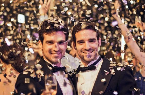Two smiling men in tuxedos and bow ties celebrating the new year under falling confetti