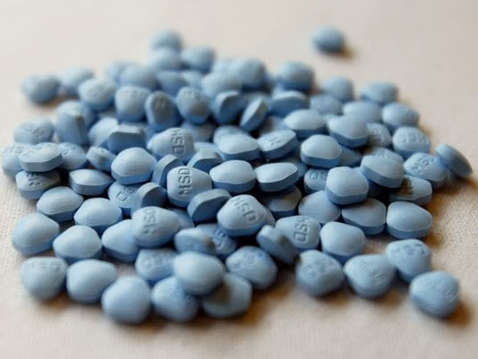 Pile of blue finasteride tablets stamped MSD on a pale surface