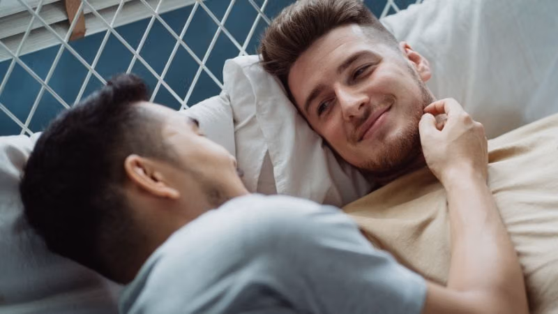 Gay couple lying close together in bed, one smiling at the other