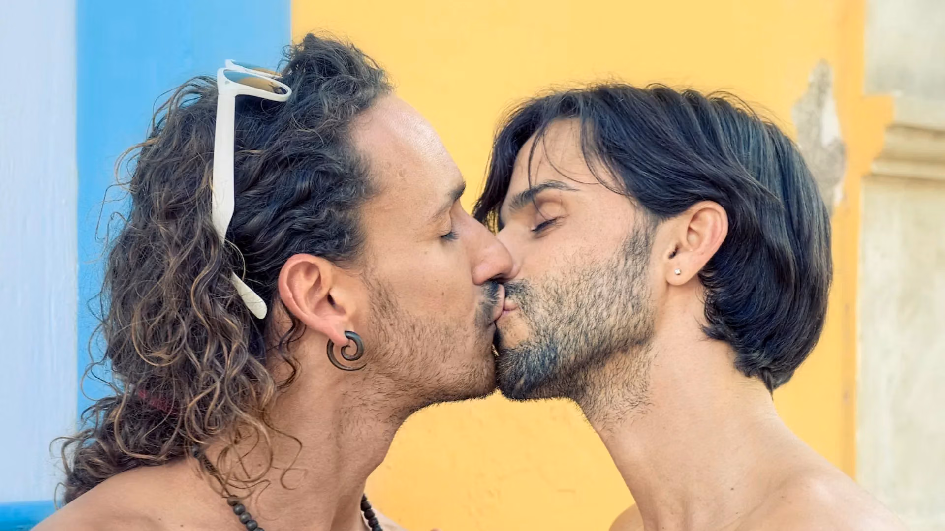 Gay couple kissing in front of a bright yellow and blue wall