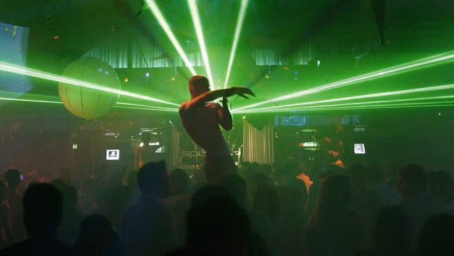 Shirtless dancer under green lasers above a packed nightclub crowd