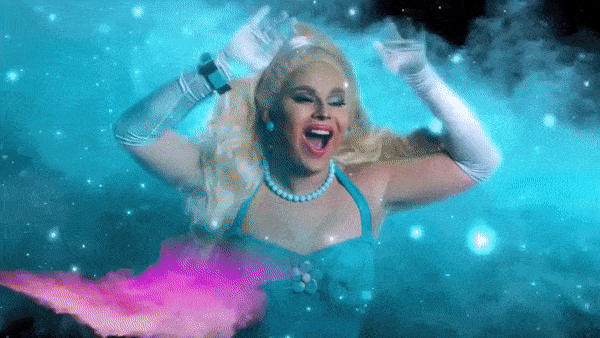 Blonde drag queen in a teal dress, pearls and white gloves dancing in swirling blue smoke