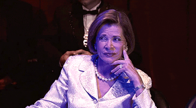 A woman in pearls and a white suit gives a skeptical side-eye