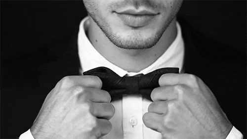 Black-and-white close-up of a man straightening his black bow tie