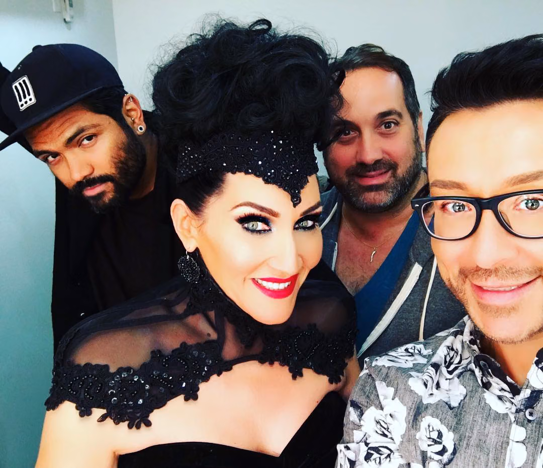 Michelle Visage in her black lace collar and tall updo, posing for a backstage selfie with three men