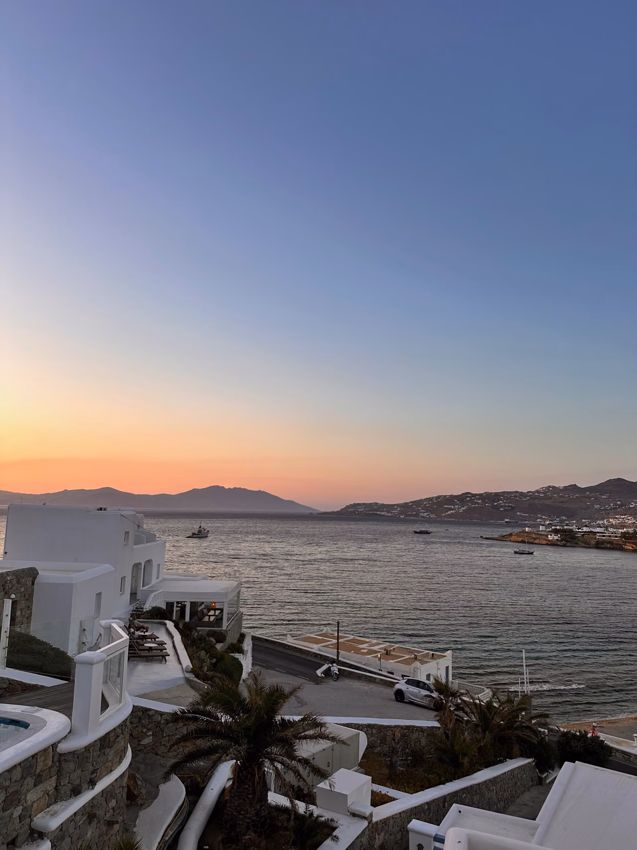 Pink evening sky above the sea and white terraces at Grand Beach Mykonos.