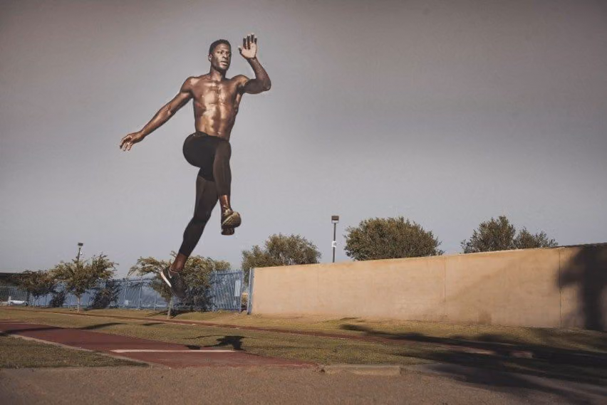Shirtless athlete leaps high in mid-stride above an outdoor running track