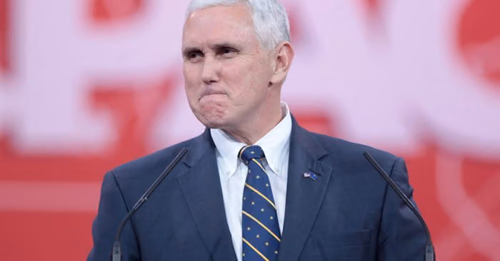Mike Pence pressing his lips together at a podium with microphones