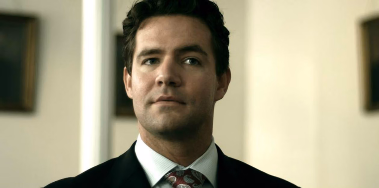 Ben Bennett, the small-town attorney in Before the Fall, wearing a dark suit and red paisley tie