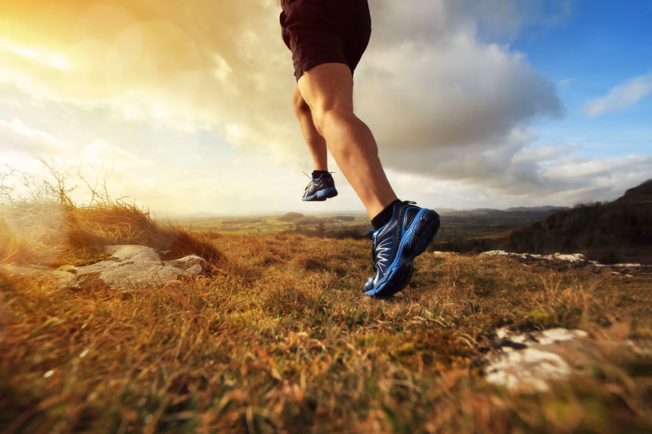 Runner's legs mid-stride on a grassy hilltop at sunrise