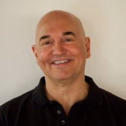 Headshot of John-Manuel Andriote smiling in a black polo shirt