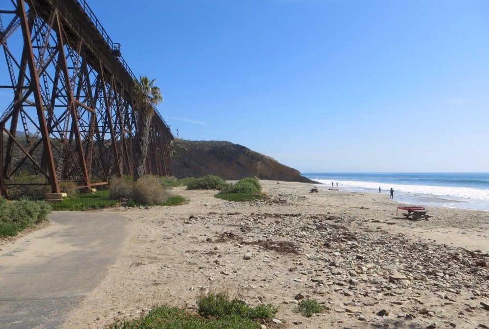 Rusty railroad trestle and a palm tree beside the rocky sand of Gaviota State Beach