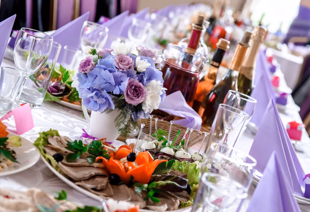 Wedding reception table with lavender napkins, purple flowers, wine bottles and cold-cut platters