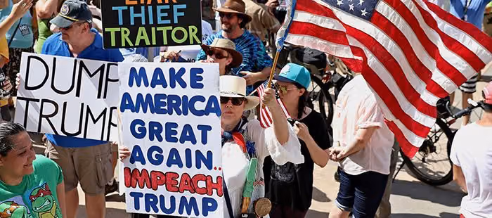 Protesters with an American flag and signs reading Dump Trump and Make America Great Again, Impeach Trump