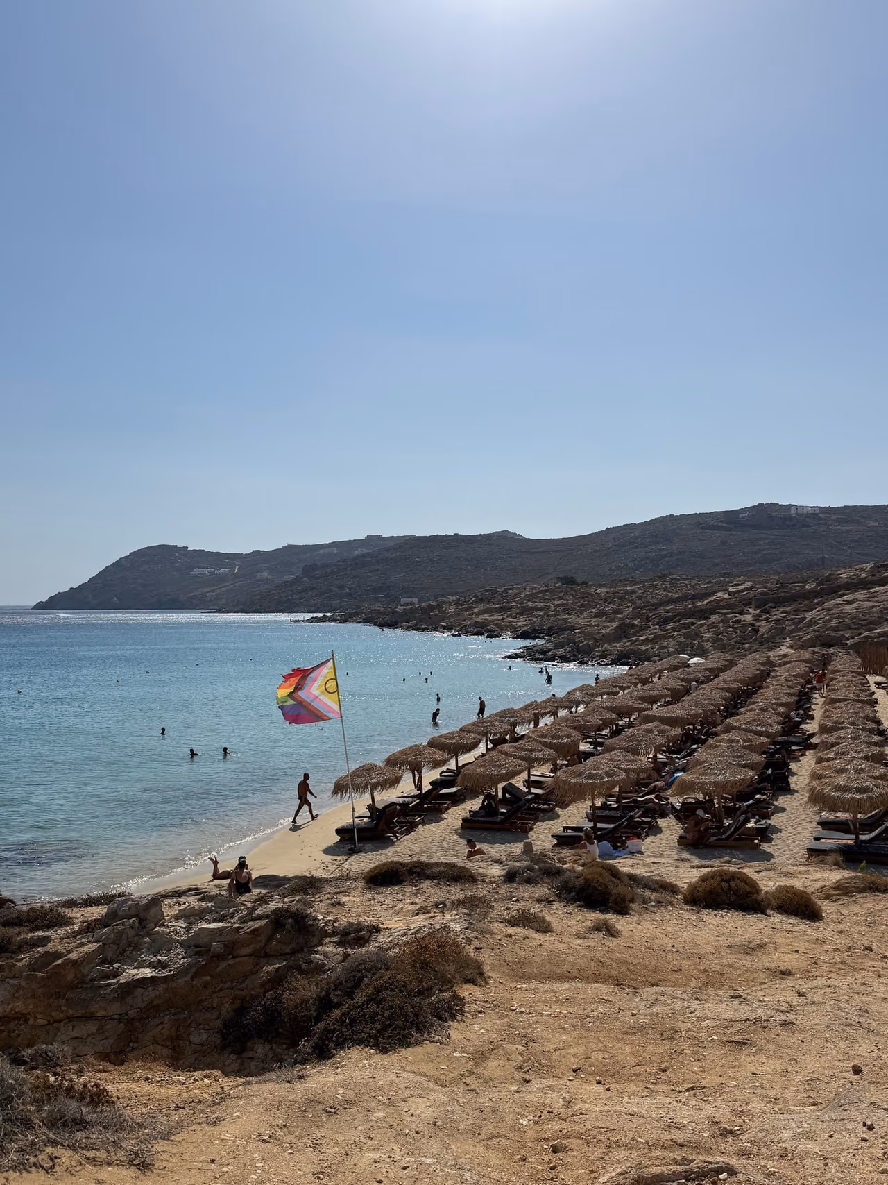 Rainbow flag above rows of sun loungers and umbrellas at Elia Beach.
