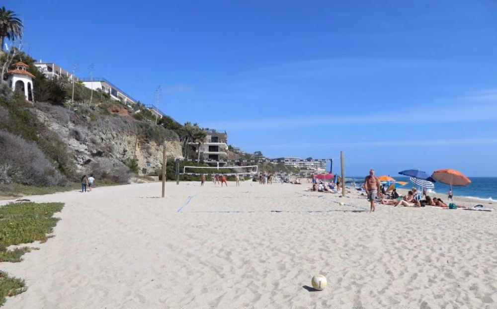 Sunbathers, umbrellas and a volleyball net on West Street Beach below Laguna Beach cliffs