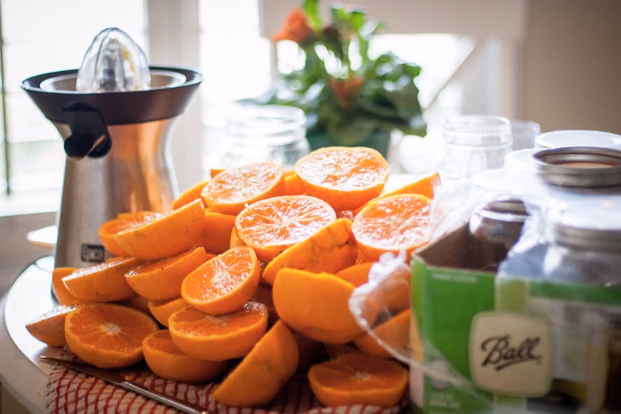 Pile of halved oranges beside a citrus juicer and mason jars, ready for fresh juice