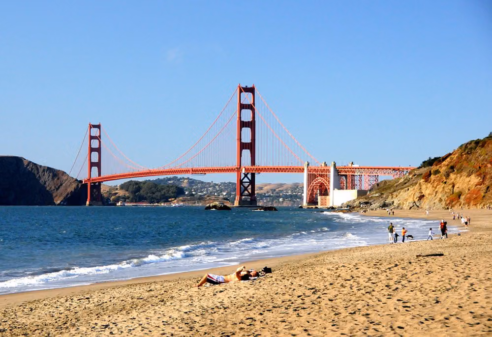 Golden Gate Bridge seen from Baker Beach, with a sunbather and walkers along the shoreline