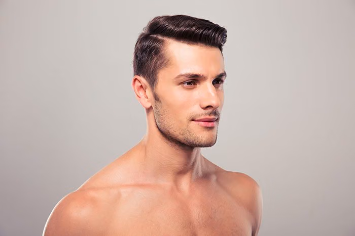 Shirtless young man with a defined jawline and light stubble, looking off to the side
