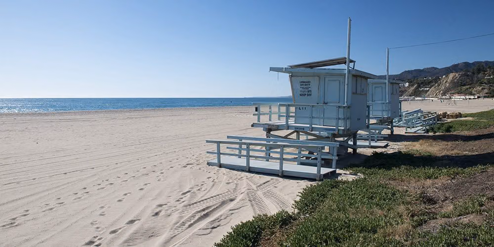 Lifeguard towers on the wide, empty sand of Will Rogers State Beach under a clear blue sky