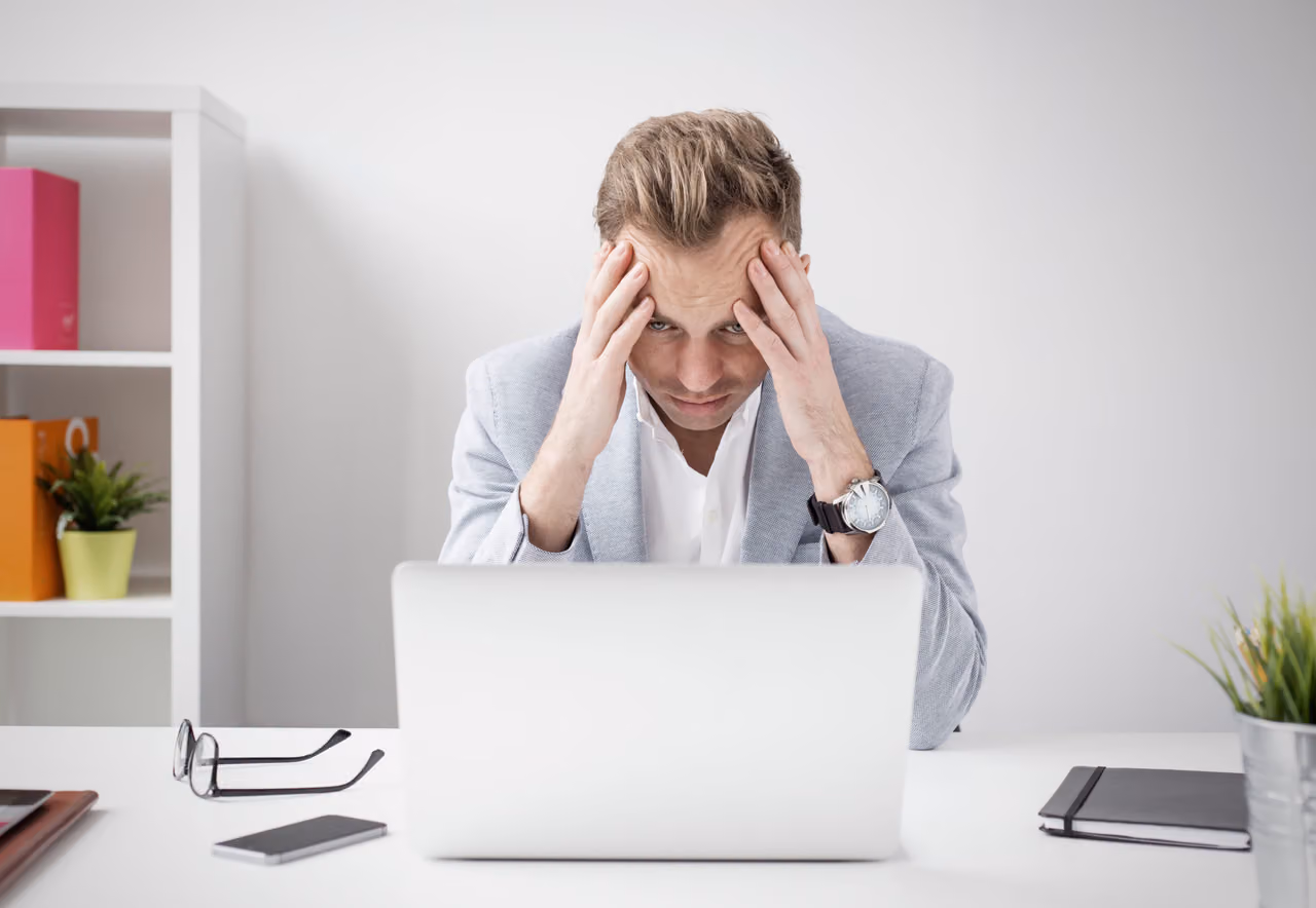 Stressed man in a blazer holds his head in his hands while staring at his laptop