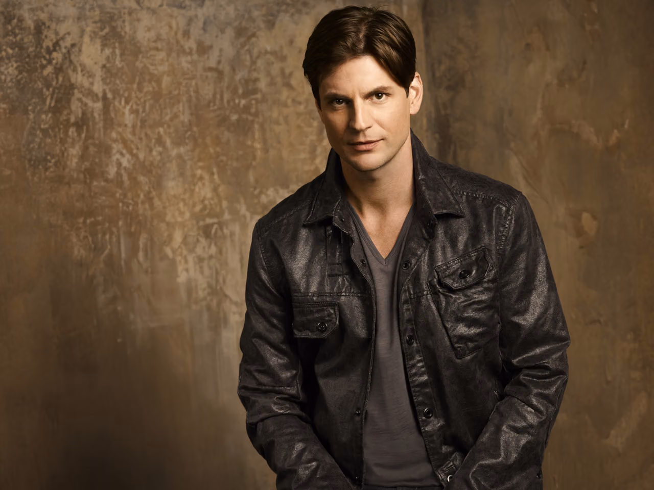 Brian Kinney of Queer As Folk in a black leather jacket against a weathered brown backdrop