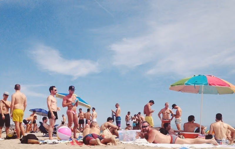 Crowd of men in swimsuits on the sand at Will Rogers State Beach under colorful umbrellas