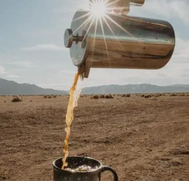 chrome coffee holder pouring coffee into a mug in the desert