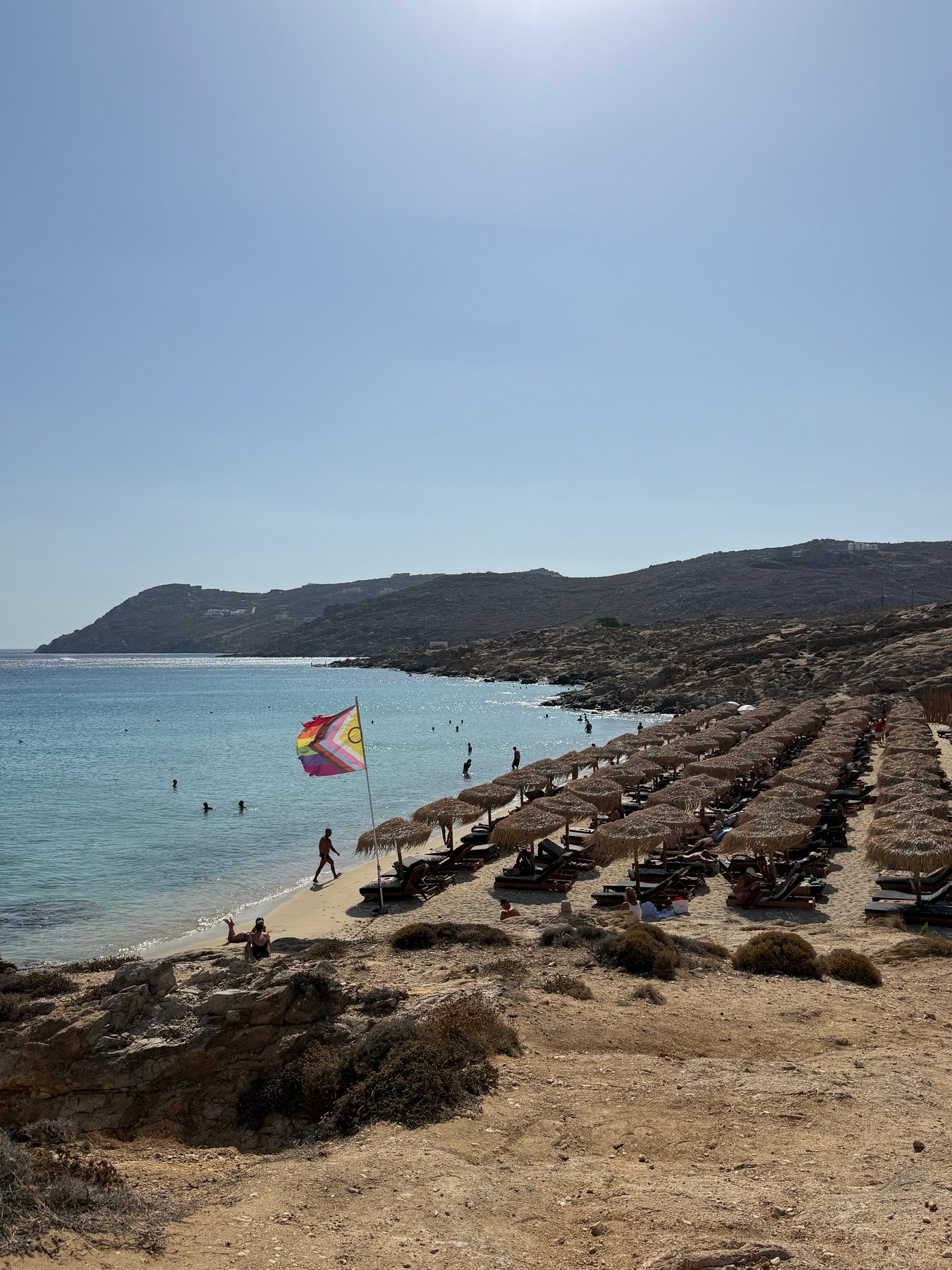 Rainbow flag above rows of sun loungers and umbrellas at Elia Beach.