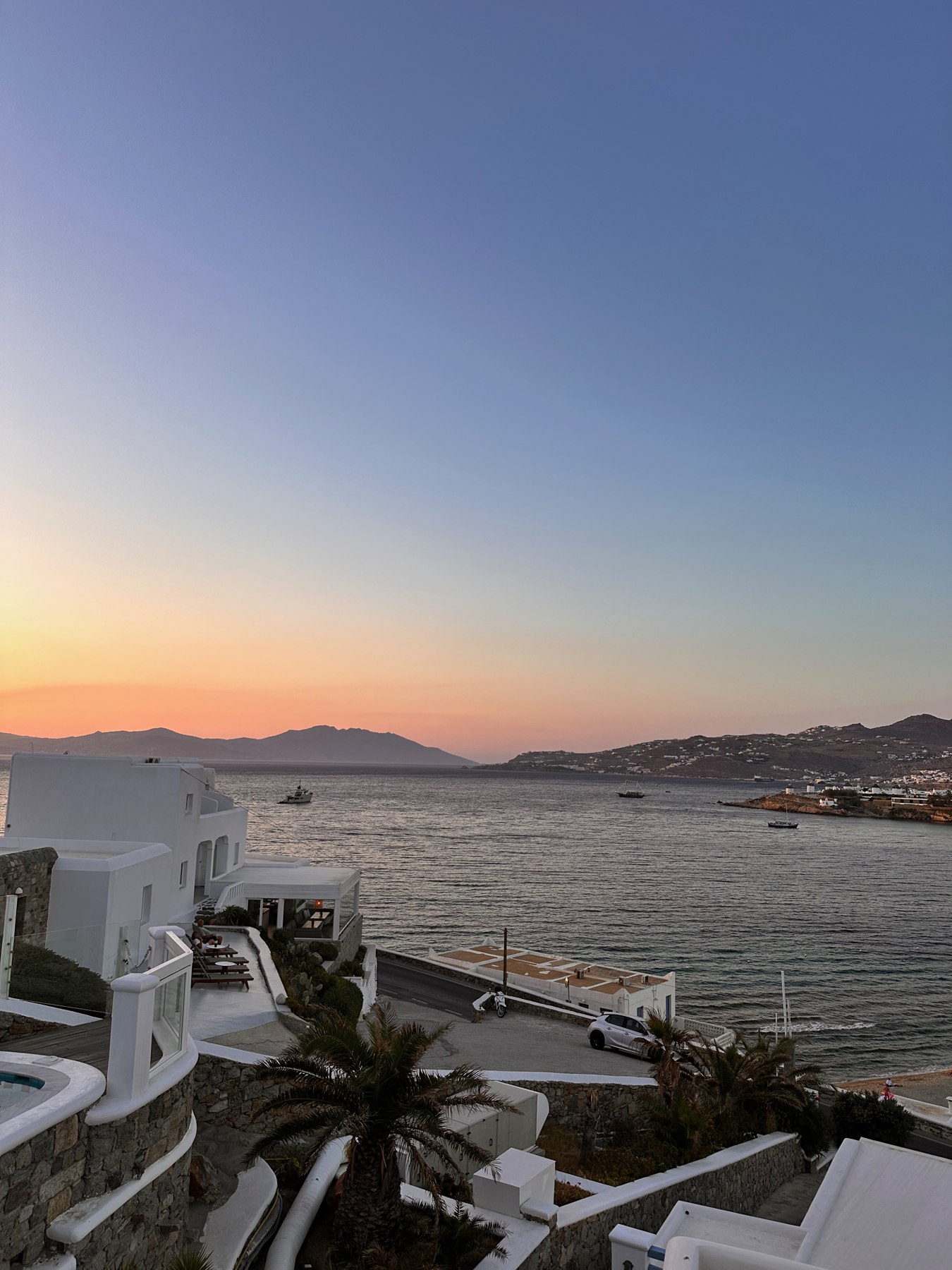 Pink evening sky above the sea and white terraces at Grand Beach Mykonos.