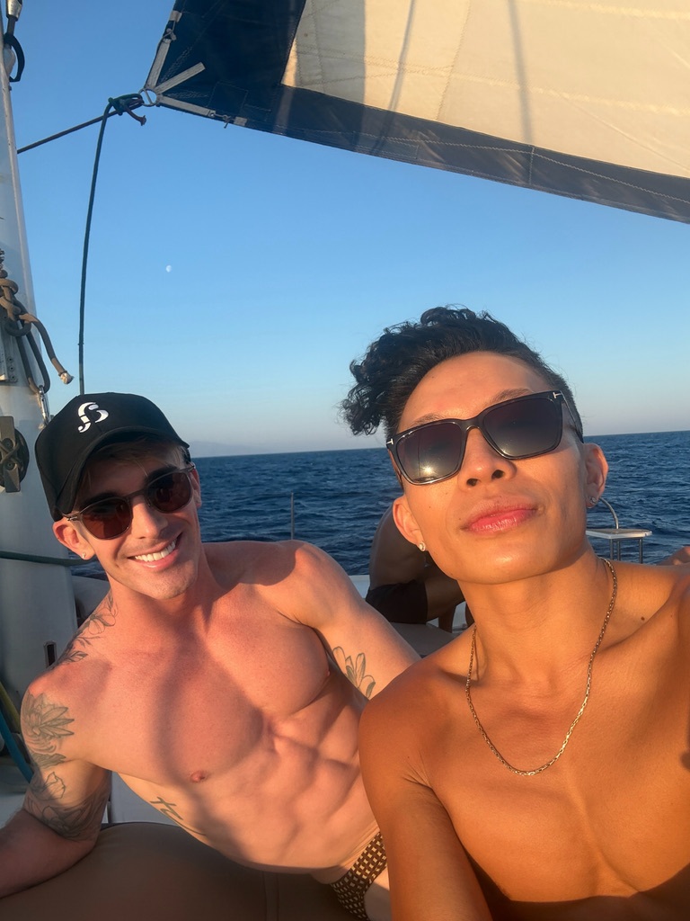 Mark in a black cap and Beatus taking a selfie beneath the catamaran sail.